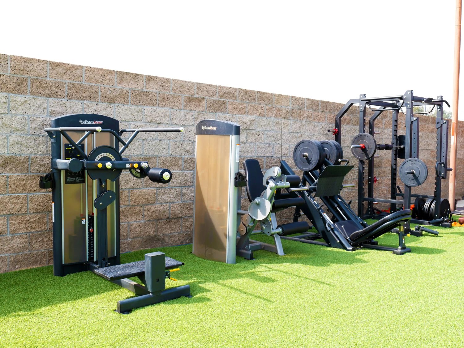 BodyKore commercial gym equipment — An outdoor strength area on turf. Selectorized machines, leg press and